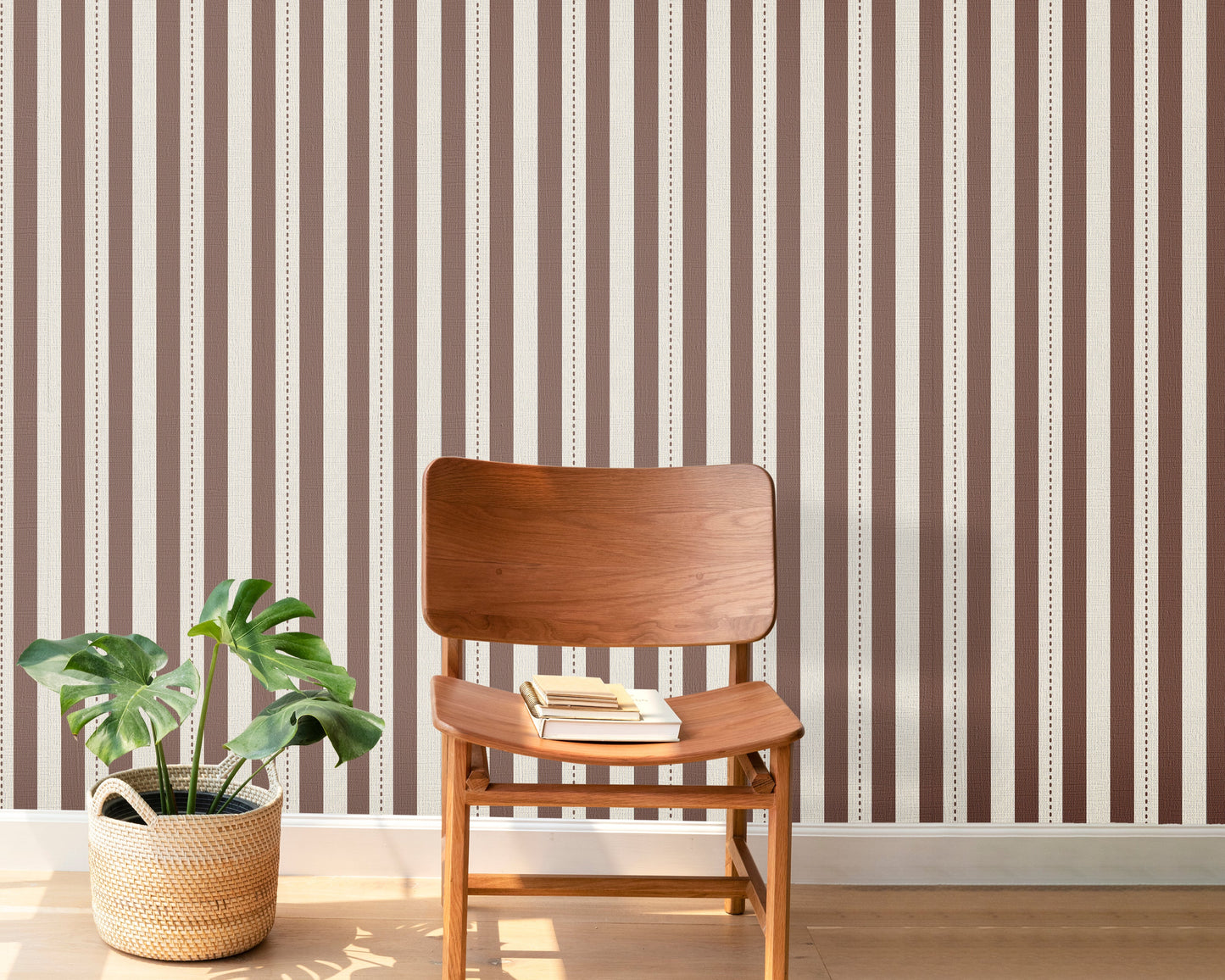 A warm, stylized workspace features a bold black and beige striped wallpaper.
The detailed design shows alternating vertical black bands and warm beige stripes.
In front, a light wood sawhorse desk table holds an assortment of books and office supplies.
The creative interior setup is completed with a black industrial pendant light and a stool.