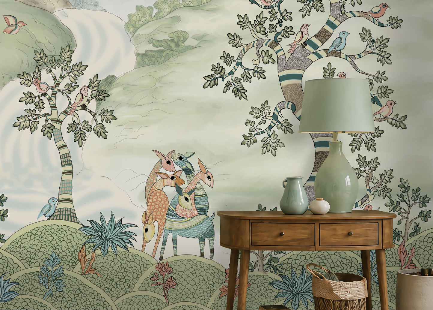 Pastel woodland wall mural featuring hand-painted sage green trees, birds in flight, and deer in a serene forest landscape, styled in a cozy living room with a green armchair and wooden console table.
