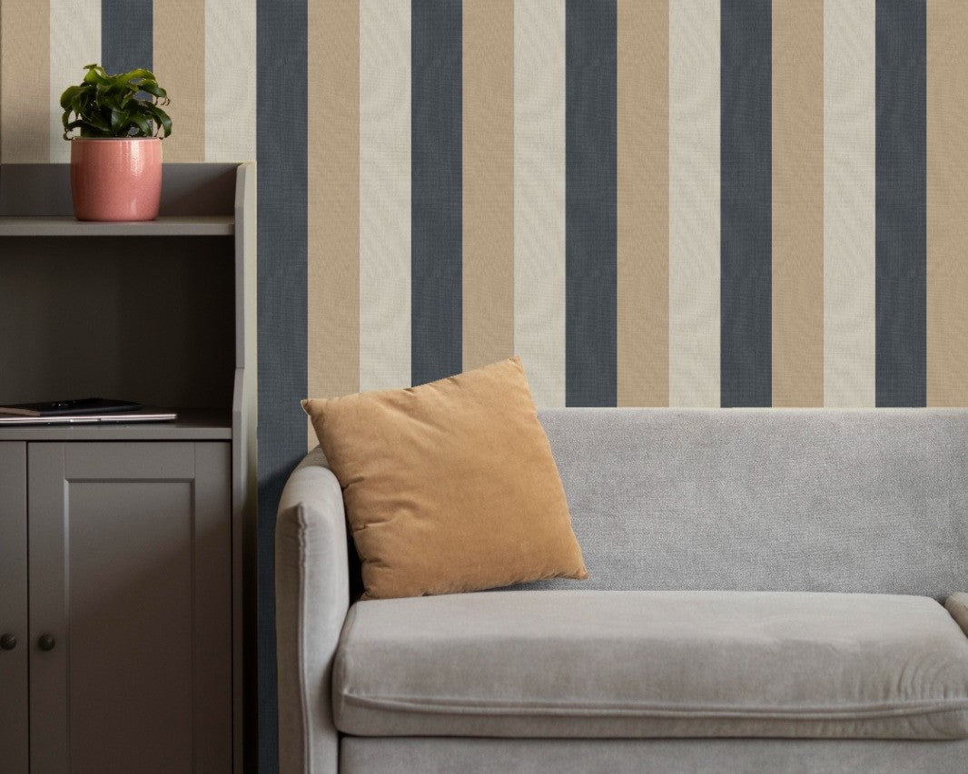 A cozy living room setup features a bold striped wallpaper with a fabric-textured look.
The design displays alternating thick vertical bands of charcoal grey, warm beige, and light cream.
In front, a comfortable light grey fabric sofa with a tan accent pillow is positioned on the right.
The modern interior space is completed by a dark grey wooden storage cabinet placed on the left side.
