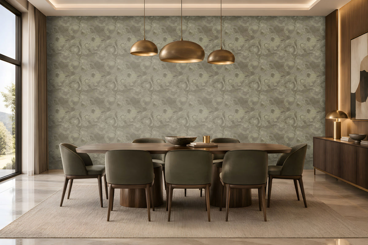 A spacious modern dining room featuring a large accent wall decorated with seamless floral swirl wallpaper in muted olive grey, soft sage, and warm taupe tones. The intricate repeating floral pattern adds depth, texture, and understated elegance to the interior. A rich dark wooden dining table paired with plush olive grey upholstered chairs complements the wallpaper beautifully, while elegant brass pendant lights, warm wooden cabinetry, and soft ambient lighting create a sophisticated atmosphere.