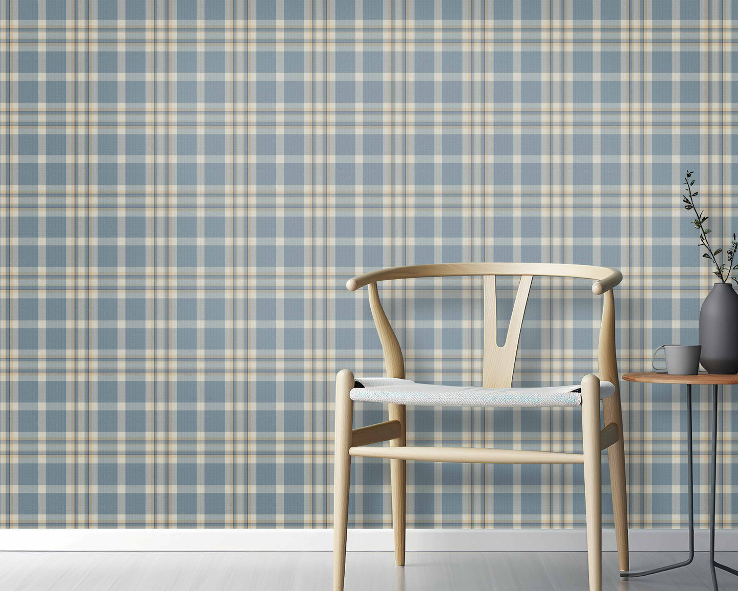 A cozy interior space features a classic plaid wallpaper in denim blue and sand tones.
The textured design displays a detailed grid pattern with intersecting blue, beige, and cream lines.
In front, a minimalist light-colored wooden wishbone chair with a woven seat is centered.
The simple setting is subtly completed by a small round side table holding a dark grey vase.