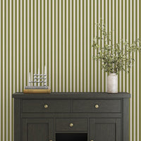 A bright dining area features a soft moss green and white striped wallpaper.
The clean design shows vertical green lines repeating across a textured white base.
In front, a warm wooden table is set with minimalist black chairs.
The sophisticated setup is completed by a contemporary black pendant light hanging above.
