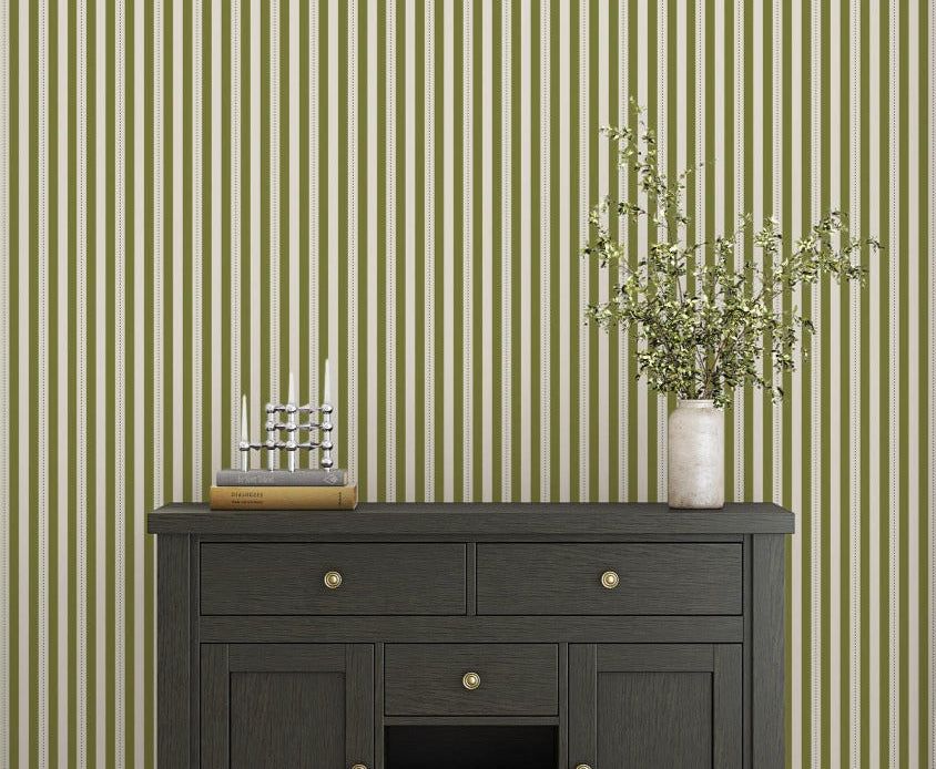 A bright dining area features a soft moss green and white striped wallpaper.
The clean design shows vertical green lines repeating across a textured white base.
In front, a warm wooden table is set with minimalist black chairs.
The sophisticated setup is completed by a contemporary black pendant light hanging above.