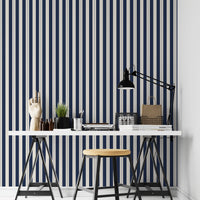 A structured workspace features a striking midnight blue and cream striped wallpaper.
The detailed design shows bold vertical navy bands and cream stripes with thin dotted lines.
In front, a clean white desktop is arranged with stationery, books, and a small green plant.
The contemporary, organized setup is uniquely accented by a decorative wooden hand model.