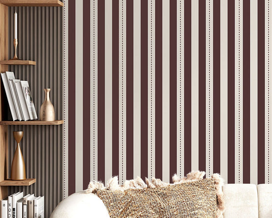 A creative workspace features a bold dark mahogany brown and beige striped wallpaper.
The detailed design shows clean vertical brown bands alongside beige stripes with thin dotted lines.
In front, a light wood desk table is neatly arranged with books, office supplies, and a clock.
The structured setup is grounded with a modern black stool and storage organizers.