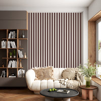 A creative workspace features a bold dark mahogany brown and beige striped wallpaper.
The detailed design shows clean vertical brown bands alongside beige stripes with thin dotted lines.
In front, a light wood desk table is neatly arranged with books, office supplies, and a clock.
The structured setup is grounded with a modern black stool and storage organizers.