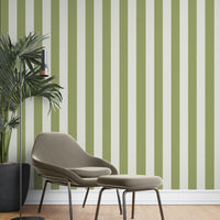 A cozy reading corner features a striped wallpaper pattern.
The wallpaper colors are an olive green and crisp white.
The design has clean, evenly spaced vertical stripes across the wall.
A modern taupe armchair sits in the center with a matching ottoman.
A tall black floor lamp stands next to a large potted plant.
The look is finished with light wood flooring and a white baseboard.