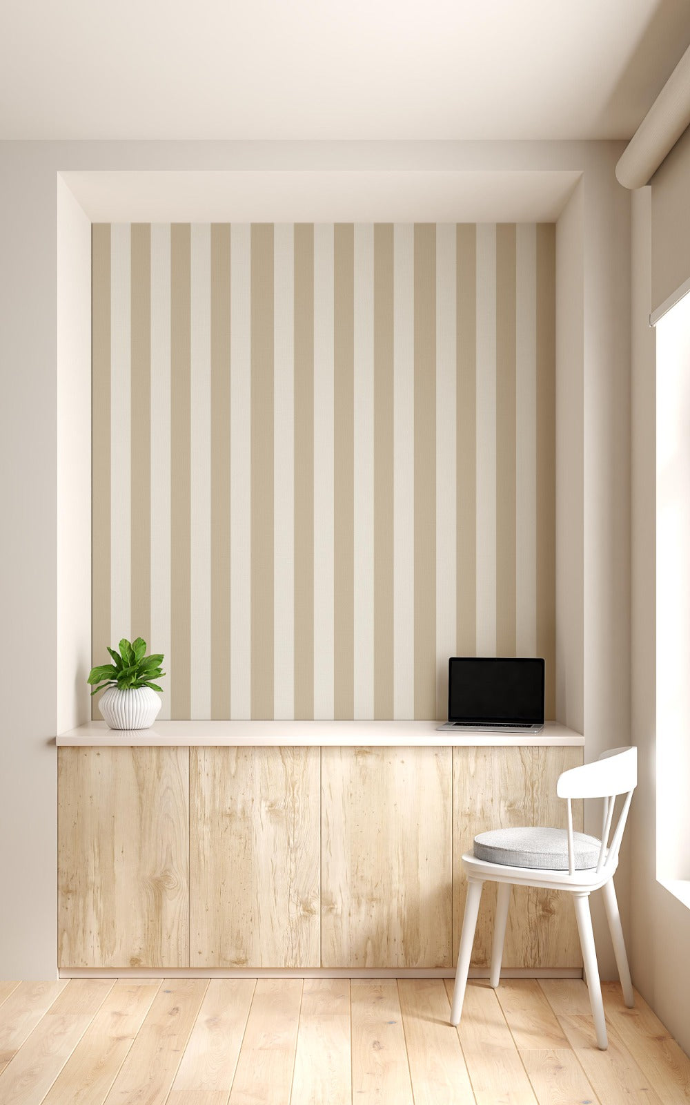 A compact workspace nook features a vertical striped wallpaper pattern.
The wallpaper colors are a muted almond beige and soft cream white.
The design has clean, evenly spaced vertical stripes filling the recessed wall.
A long, built-in light wood desk cabinet sits below the wallpaper.
The desk surface holds a small potted green plant and an open laptop.
A simple white wooden chair with a grey cushion is placed nearby.