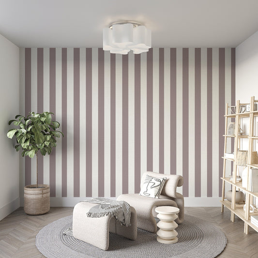 A modern living room features a muted taupe and off-white striped wallpaper.
The design showcases clean, evenly spaced vertical lines covering the main back wall.
In front, a stylish cream-colored lounge chair and matching ottoman sit on a round rug.
The minimalist space is complete with a large potted plant and a light wood bookshelf.