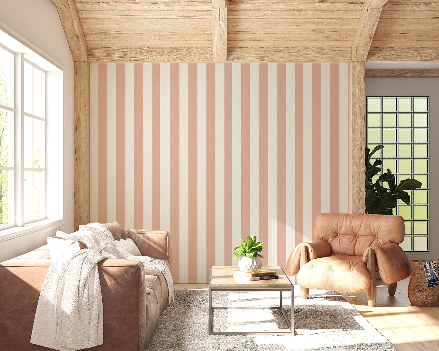 A sunlit living room features a warm honey-taupe and cream striped wallpaper.
The design showcases clean, evenly spaced vertical stripes across the central wall.
In front, a brown leather sofa and matching armchair frame a small coffee table.
The rustic space is complete with a textured area rug and a light wood beamed ceiling.