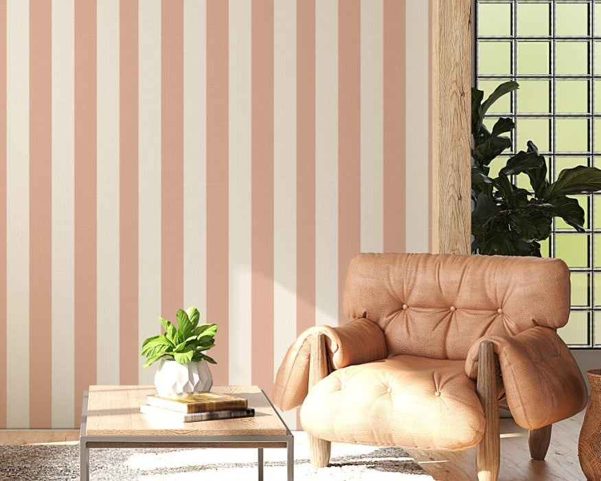 A sunlit living room features a warm honey-taupe and cream striped wallpaper.
The design showcases clean, evenly spaced vertical stripes across the central wall.
In front, a brown leather sofa and matching armchair frame a small coffee table.
The rustic space is complete with a textured area rug and a light wood beamed ceiling.