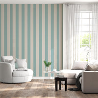 A sunlit living room features a soft sage blue and warm cream striped wallpaper.
The design showcases clean, evenly spaced vertical stripes filling the central accent wall.
In front, a rounded white armchair and a light grey sectional sofa face each other.
The bright, modern space is complete with natural wood flooring and sheer white curtains.