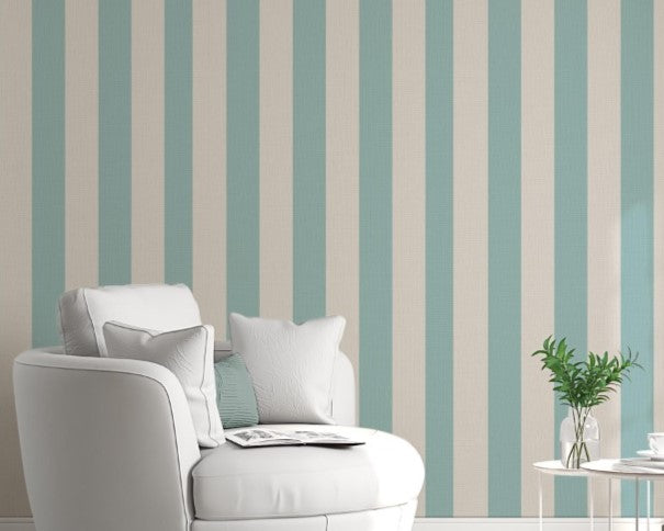 A sunlit living room features a soft sage blue and warm cream striped wallpaper.
The design showcases clean, evenly spaced vertical stripes filling the central accent wall.
In front, a rounded white armchair and a light grey sectional sofa face each other.
The bright, modern space is complete with natural wood flooring and sheer white curtains.