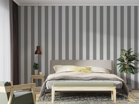 A modern bedroom features a simple grey and white striped wallpaper.
The design showcases clean, evenly spaced vertical stripes filling the main wall.
In front, a fully dressed bed with a fabric headboard centers the cozy setup.
The styled space is finished with a wooden bench, a side table, and a green plant.