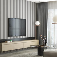 A stylish living room features a dark chocolate brown and crisp white striped wallpaper.
The design showcases clean, evenly spaced vertical stripes across the expansive back wall.
In front, a plush cream-colored sofa and matching armchair frame sleek round coffee tables.
The modern, high-contrast space is complete with a geometric area rug and potted green plants.