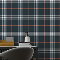 A sleek home office features a dark midnight blue and white plaid wallpaper.
The detailed design shows intersecting white and orange lines forming grids over a dark base.
In front, a simple black desk setup holds a modern table lamp and stationery.
The organized workspace is cleanly finished with a matching black office chair.