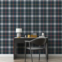 A sleek home office features a dark midnight blue and white plaid wallpaper.
The detailed design shows intersecting white and orange lines forming grids over a dark base.
In front, a simple black desk setup holds a modern table lamp and stationery.
The organized workspace is cleanly finished with a matching black office chair.