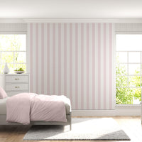 A bright bedroom features a soft pink and white vertically striped wallpaper.
The detailed design shows thin, evenly spaced pink stripes running down a white base.
In front, a neatly made bed with a light pink comforter rests near a matching nightstand.
The relaxing space is complete with two light grey dressers, large windows, and a rug.