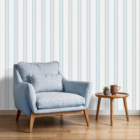 A bright sitting area features a clean coastal dune blue and white striped wallpaper.
The detailed design shows thin blue and beige vertical stripes repeating down a light base.
In front, a plush light blue armchair with a matching lumbar pillow rests comfortably.
The relaxing space is complete with a small wooden side table holding a mug and plant.
