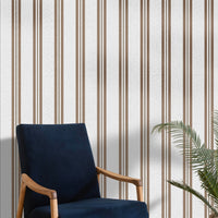 A bright seating area features a warm rustic mocha brown and white striped wallpaper.
The detailed design shows clean brown vertical lines repeating across a textured light base.
In front, a classic dark blue velvet armchair with a wooden frame sits comfortably.
The simple, inviting space is naturally accented with a leafy green potted plant nearby.
