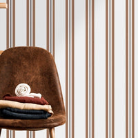 A warm dining area features a soft brown and white striped wallpaper.
The clean design shows vertical light brown lines repeating across a cream base.
In front, a sleek dark wooden table is paired with minimalist black chairs.
The sophisticated setup is completed by a contemporary black pendant light hanging above.