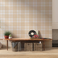 A stylish living area features a warm golden yellow and white plaid wallpaper.
The detailed design shows thin white lines intersecting to form clean grids across a yellow base.
In front, a cream-colored wooden sideboard with woven rattan doors is centered nicely.
The bright setup is accented with a white desk lamp, pottery, and a leafy green plant.