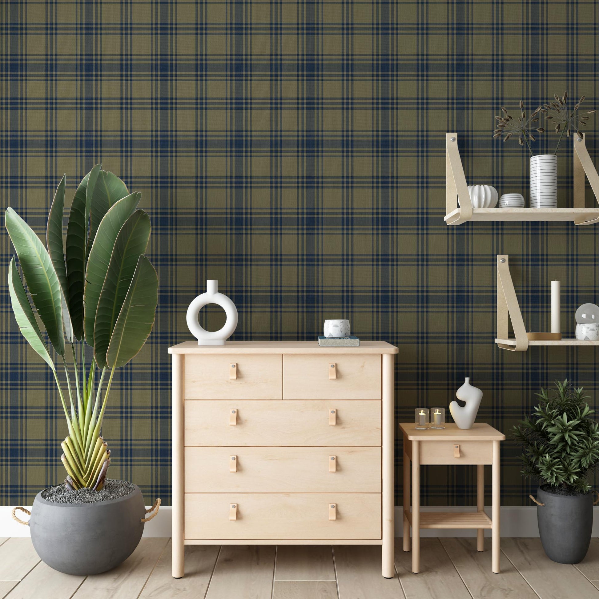 A cozy room features a dark olive green and navy blue plaid wallpaper.
The detailed design shows intersecting dark stripes over a muted green base.
In front, a light wood chest of drawers stands next to a small matching side table.
The rustic space is accented with large potted plants and minimalist wall shelves.