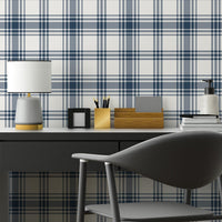 A clean workspace setup features a classic navy blue and white plaid wallpaper.
The detailed design shows intersecting dark blue stripes forming grids on a white base.
In front, a sleek dark grey desk holds a small lamp, notebooks, and office accessories.
A modern dark grey desk chair with a rounded back completes the organized study area.