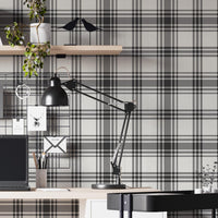 A modern home office features a classic charcoal grey and off-white plaid wallpaper.
The detailed pattern shows intersecting dark lines creating a clean grid on a light base.
In front, a sleek white study desk setup holds a laptop, lamp, and floating bookshelf.
The organized workspace is complete with a black office chair and a rolling utility cart.