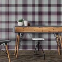 A cozy bedroom features a rich mulberry purple and beige plaid wallpaper.
The detailed pattern shows intersecting dark purple lines forming a clean grid on a light base.
In front, a neatly made bed with a dark purple comforter centers the stylish room.
A simple black wire-frame side table holding a single flower completes the minimalist setup.