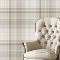 A classic interior scene featuring a beige tufted armchair with dark wooden legs placed against a neutral plaid wallpaper in soft taupe and cream tones. The room has white painted wood flooring and a calm, elegant aesthetic.