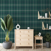An indoor shot showcases a chest of drawers, a side table, a wall shelf, and plants positioned against a green checkered wall. The light-colored wooden chest of drawers, situated in the center, features four tiers of drawers, with the top tier split into two smaller drawers. All drawers are equipped with small, light brown leather handles. On top of the chest of drawers rests a circular white vase and a small white mug. 