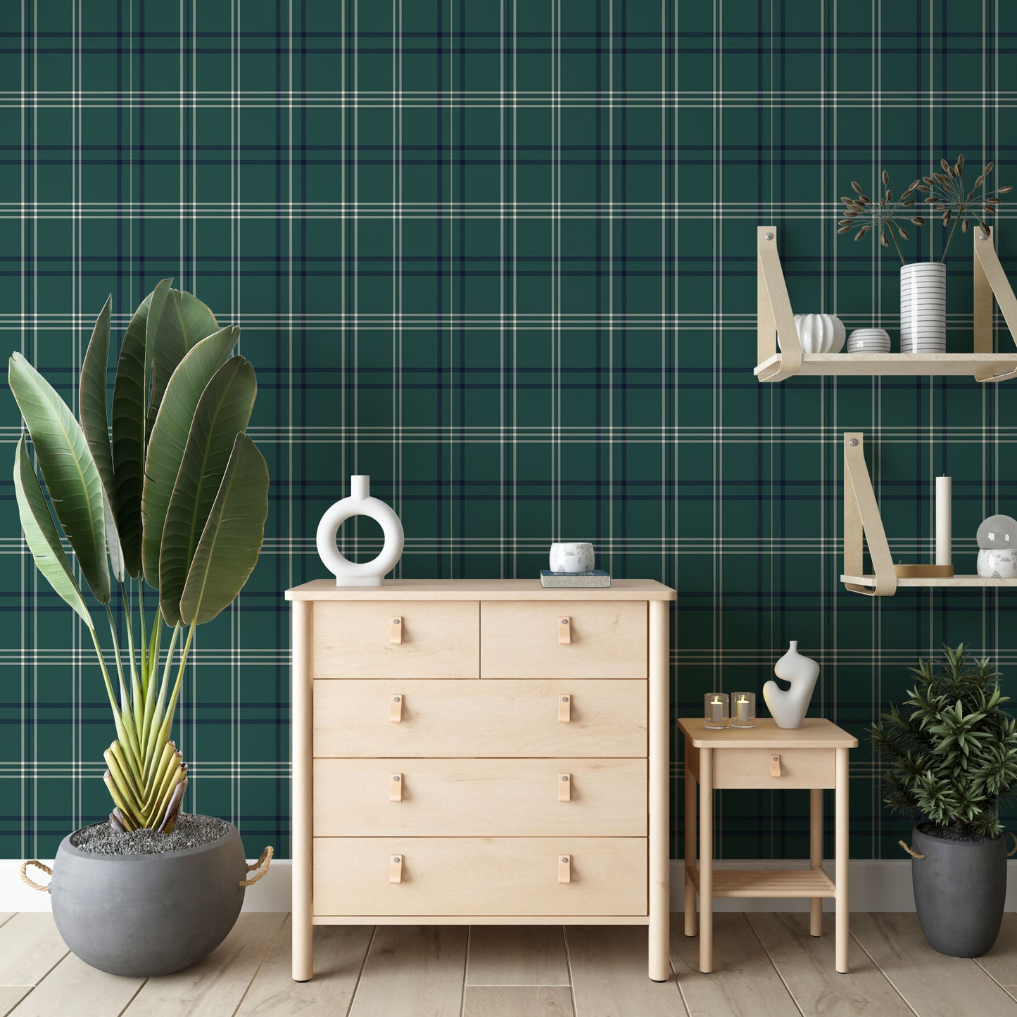 An indoor shot showcases a chest of drawers, a side table, a wall shelf, and plants positioned against a green checkered wall. The light-colored wooden chest of drawers, situated in the center, features four tiers of drawers, with the top tier split into two smaller drawers. All drawers are equipped with small, light brown leather handles. On top of the chest of drawers rests a circular white vase and a small white mug. 