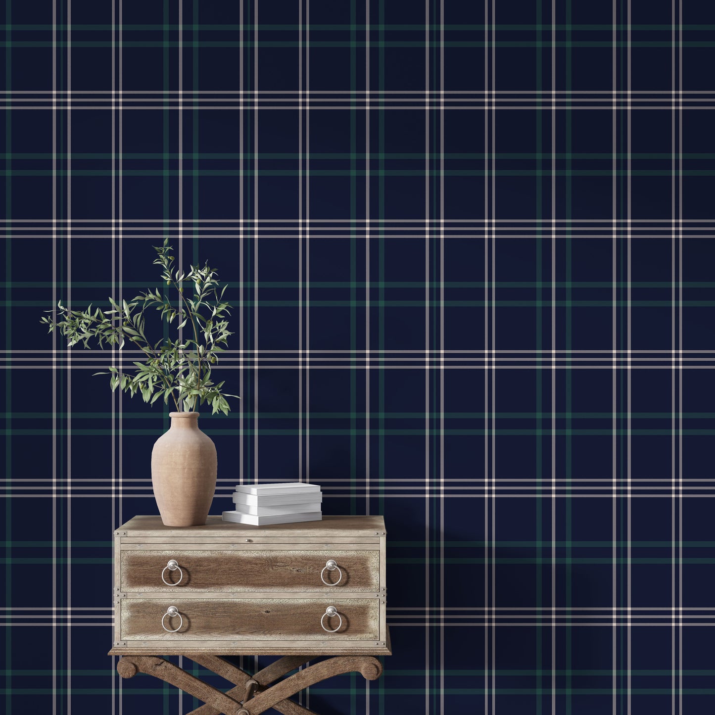 An interior setting highlights a dark navy blue wallpaper with a classic green and white plaid pattern.
In the foreground, a rustic light wood chest or table sits with subtle metal rivets along its top edge.
A large, textured terracotta vase with a rounded body rests on the left side of the wooden surface.
The vase is filled with leafy olive branches extending upwards, adding a vibrant touch of natural green.