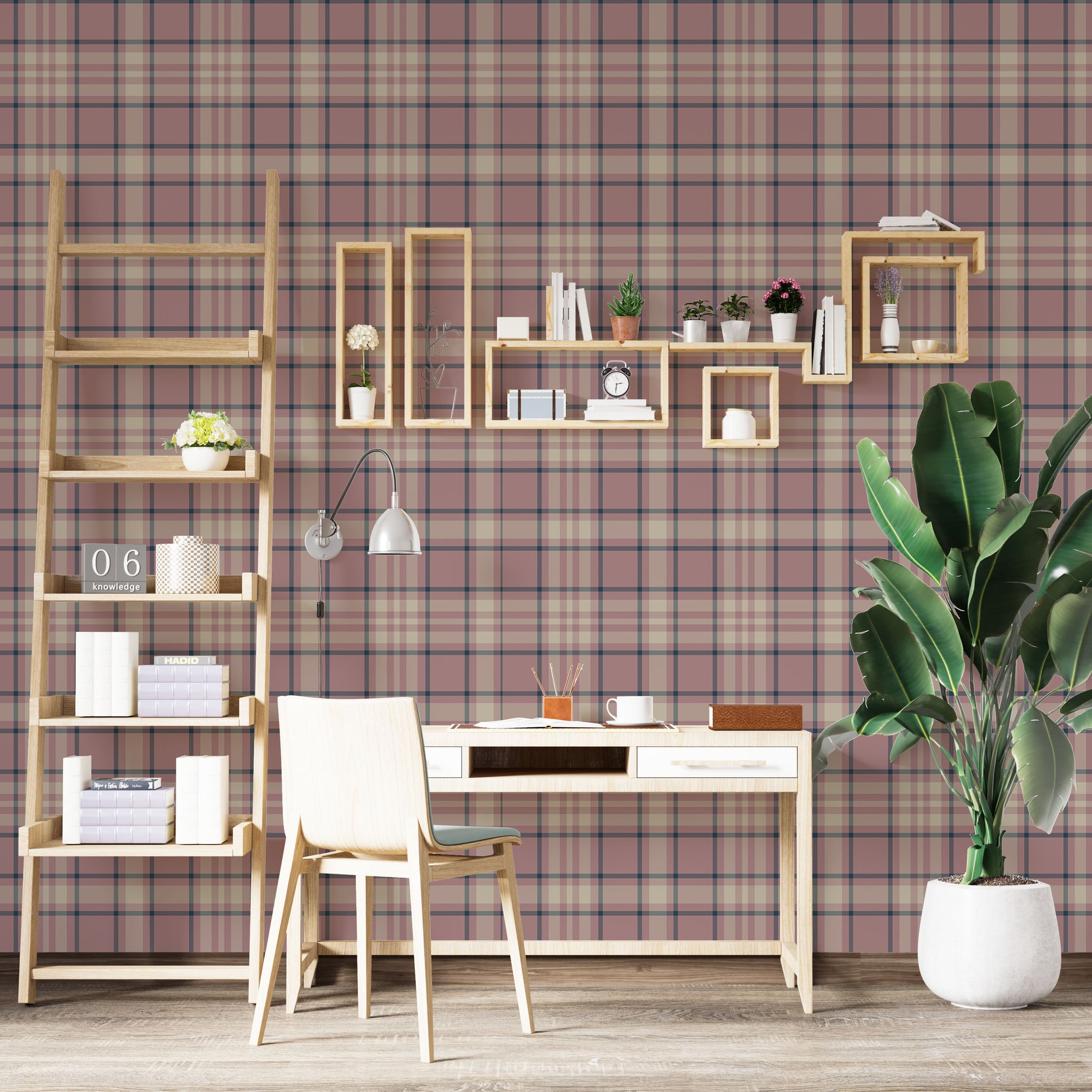 A modern living space featuring a warm desert-blush pink and white plaid wallpaper accent wall. In the center, a light oak sideboard cabinet with wooden legs holds a small wooden tripod lamp, a geometric candle, and a round white ceramic vase with a single sprig of dried pampas grass. To the left, a woven basket sits on the light wood floor, filled with tall, fluffy pampas grass stalks and a draped blanket.