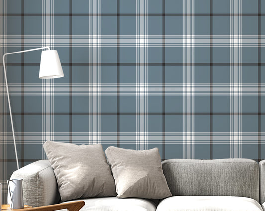 A modern living room features a serene blue-steel grey and white plaid wallpaper.
The detailed design shows intersecting white and dark lines creating grids on a blue base.
In front, a light grey fabric sofa with matching cushions sits centered in the room.
The bright space is complete with a wooden armchair, coffee tables, and a floor lamp.
