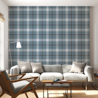 A modern living room features a serene blue-steel grey and white plaid wallpaper.
The detailed design shows intersecting white and dark lines creating grids on a blue base.
In front, a light grey fabric sofa with matching cushions sits centered in the room.
The bright space is complete with a wooden armchair, coffee tables, and a floor lamp.