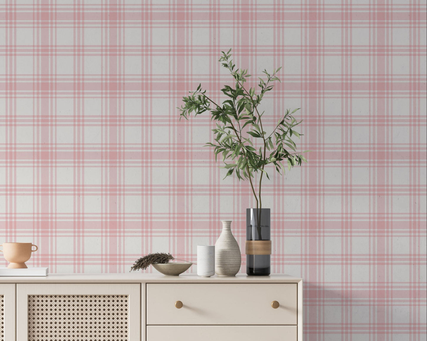 A charming living area features a soft baby pink and white plaid wallpaper.
The detailed design shows intersecting light pink lines forming grids over a light base.
In front, a cream-colored wooden sideboard with woven rattan doors is centered nicely.
The serene setup is accented with a white desk lamp, pottery, and a leafy green plant.