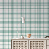 A serene living area features a soft baby green and white plaid wallpaper.
The detailed design shows intersecting light green lines forming grids over a light base.
In front, a cream-colored wooden sideboard with woven rattan doors is centered nicely.
The relaxing setup is accented with a white desk lamp, pottery, and a leafy green plant.