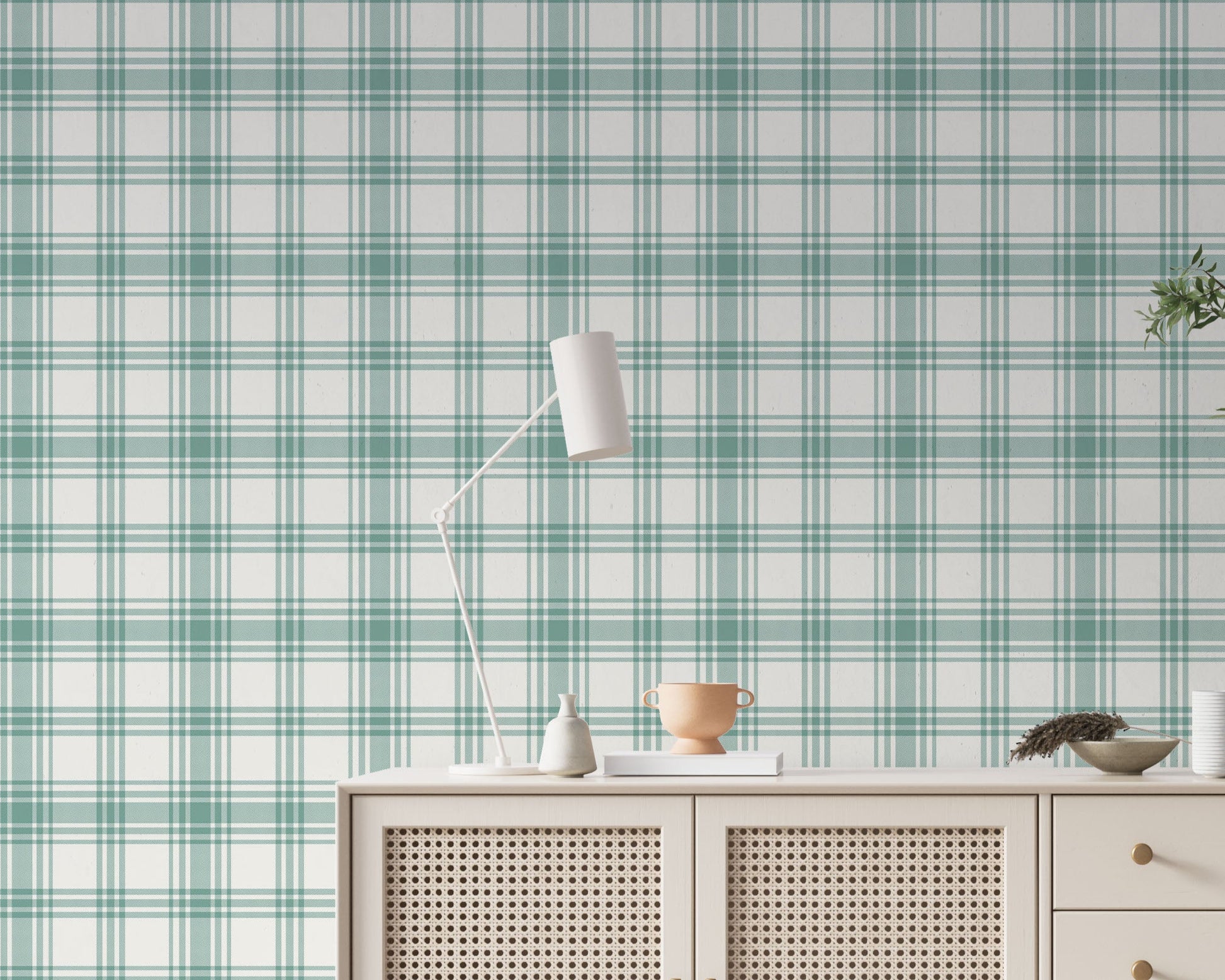 A serene living area features a soft baby green and white plaid wallpaper.
The detailed design shows intersecting light green lines forming grids over a light base.
In front, a cream-colored wooden sideboard with woven rattan doors is centered nicely.
The relaxing setup is accented with a white desk lamp, pottery, and a leafy green plant.
