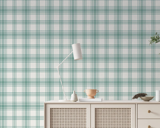 A serene living area features a soft baby green and white plaid wallpaper.
The detailed design shows intersecting light green lines forming grids over a light base.
In front, a cream-colored wooden sideboard with woven rattan doors is centered nicely.
The relaxing setup is accented with a white desk lamp, pottery, and a leafy green plant.