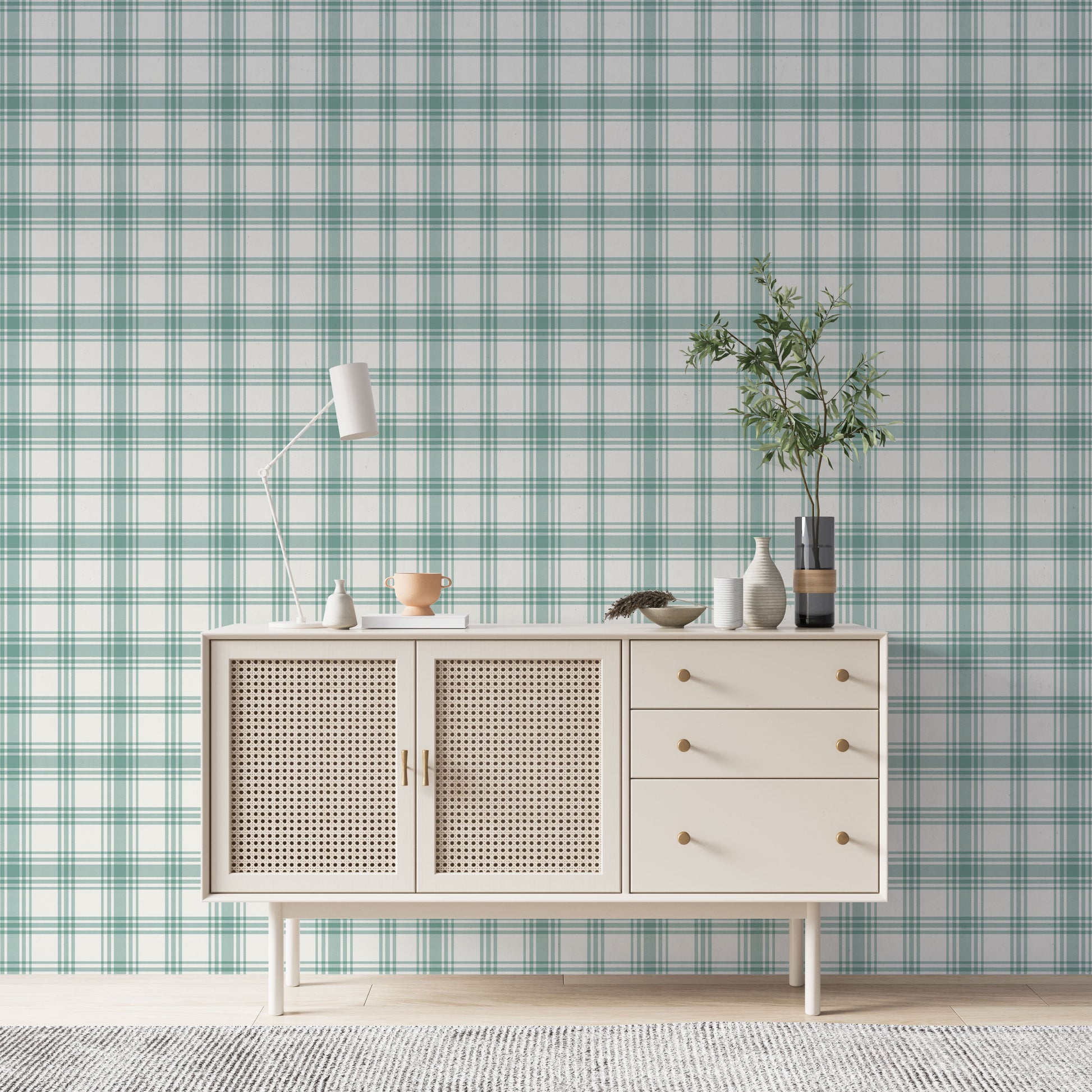 A serene living area features a soft baby green and white plaid wallpaper.
The detailed design shows intersecting light green lines forming grids over a light base.
In front, a cream-colored wooden sideboard with woven rattan doors is centered nicely.
The relaxing setup is accented with a white desk lamp, pottery, and a leafy green plant.