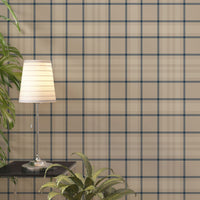 A modern living space featuring a warm soft caramel brown, beige, and cream plaid wallpaper accent wall. In the center, a light oak sideboard cabinet with wooden legs holds a small wooden tripod lamp, a geometric candle, and a round white ceramic vase with a single sprig of dried pampas grass. To the left, a woven basket sits on the light wood floor, filled with tall, fluffy pampas grass stalks and a draped blanket.