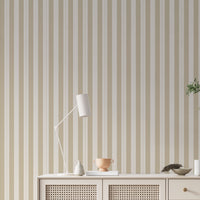 A minimalist hallway setup features a pale sand and cream striped wallpaper.
The detailed design shows clean vertical tan bands alongside cream stripes with thin dotted lines.
In front, a cream console cabinet with woven mesh doors stands against the wall.
The bright, neutral space is elegantly finished with a modern desk lamp and a leafy plant.