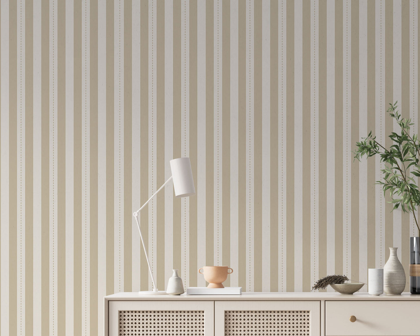 A minimalist hallway setup features a pale sand and cream striped wallpaper.
The detailed design shows clean vertical tan bands alongside cream stripes with thin dotted lines.
In front, a cream console cabinet with woven mesh doors stands against the wall.
The bright, neutral space is elegantly finished with a modern desk lamp and a leafy plant.