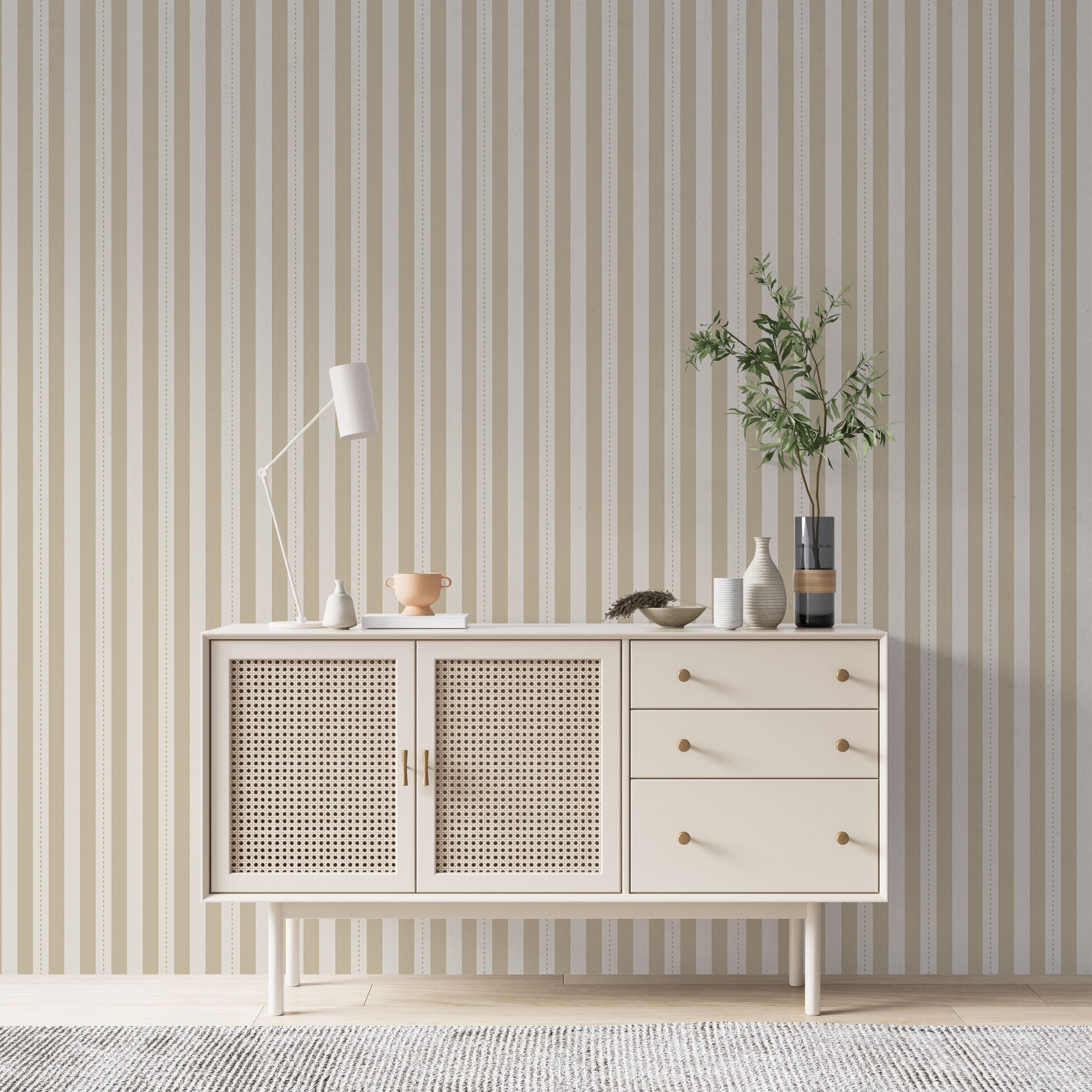 A minimalist hallway setup features a pale sand and cream striped wallpaper.
The detailed design shows clean vertical tan bands alongside cream stripes with thin dotted lines.
In front, a cream console cabinet with woven mesh doors stands against the wall.
The bright, neutral space is elegantly finished with a modern desk lamp and a leafy plant.