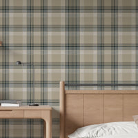 A closeup of a modern bedroom and study area featuring a prominent stone-beige plaid wallpaper. On the left, a light oak wooden desk holds a closed laptop, a small stack of books, and a sleek, matte black metal desk lamp. To the right, a matching light oak wooden headboard and bedframe are visible, with a crisp white duvet pillow and a soft beige accent pillow resting on top.