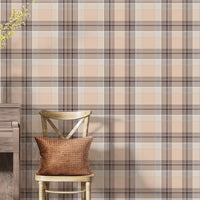 A closeup of a cozy interior setting featuring a dusty rose-pink and brown plaid wallpaper. On the left, a textured white ceramic vase with yellow flowering branches sits on top of a weathered, dark wood console table or upright piano. Next to it, a light wood cross-back dining chair holds a textured, rust-orange accent pillow.