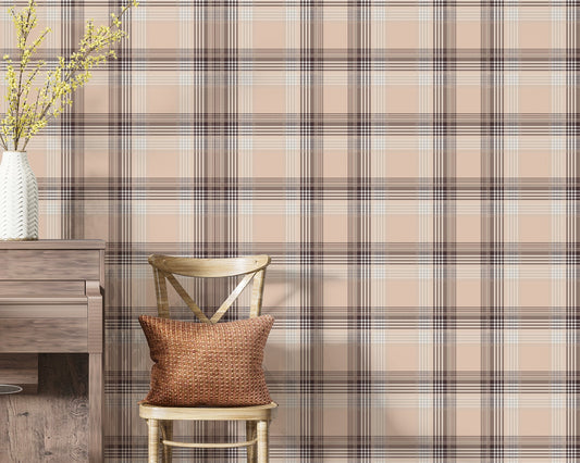 A closeup of a cozy interior setting featuring a dusty rose-pink and brown plaid wallpaper. On the left, a textured white ceramic vase with yellow flowering branches sits on top of a weathered, dark wood console table or upright piano. Next to it, a light wood cross-back dining chair holds a textured, rust-orange accent pillow.