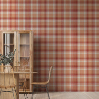 A modern dining area featuring a vibrant cinnamon-blush orange and red plaid wallpaper. On the left stands a tall, light wood display cabinet with glass doors, next to a round wooden dining table with a fluted pedestal base. Woven rattan dining chairs with slim black metal legs are arranged around the table, and a white vase filled with eucalyptus branches rests on top. The room features light-colored vertical wood plank flooring.